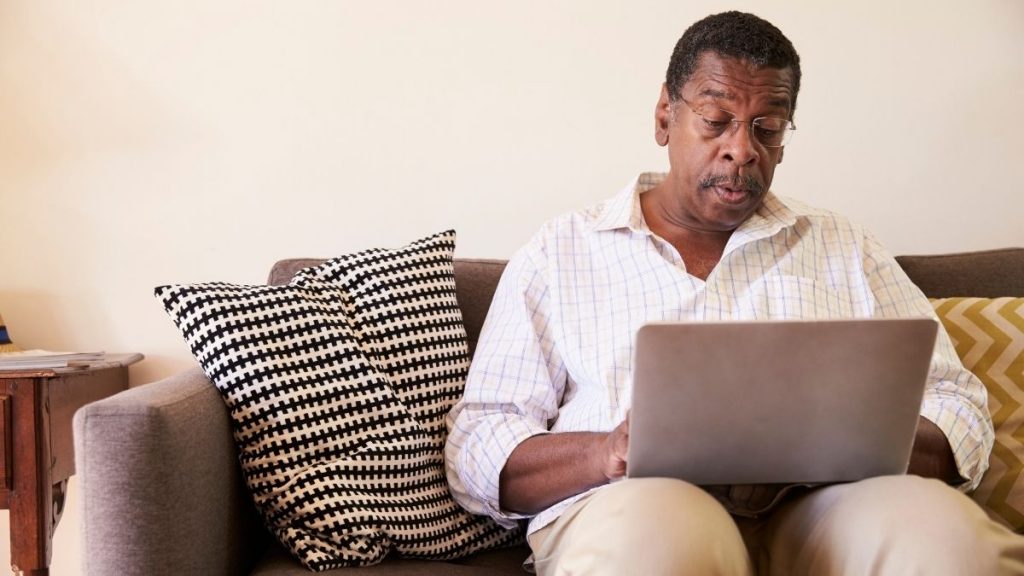 bxblue - homem negro, sentado no sofá com computador no colo - fazendo a contratação do empréstimo consignado online