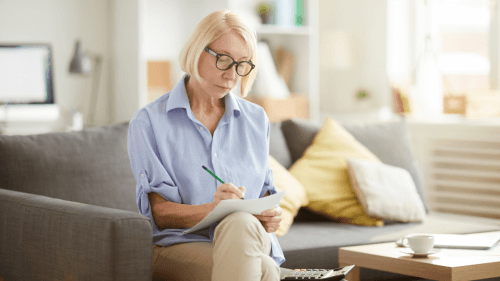 bxblue - dias do pagamento do inss - mulher com caneta e papel fazendo anotações ao lado de uma calculadora, sentada no sofá