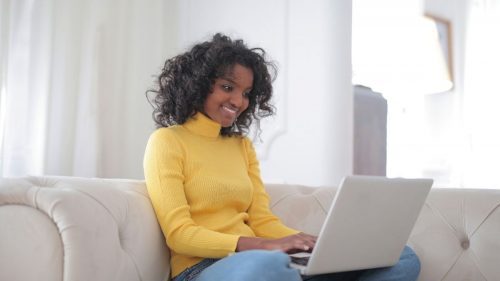 bxblue - mulher sentada no sofá com o computador no colo, fazendo pesquisa e sorrindo - bmg consignado como contratar online